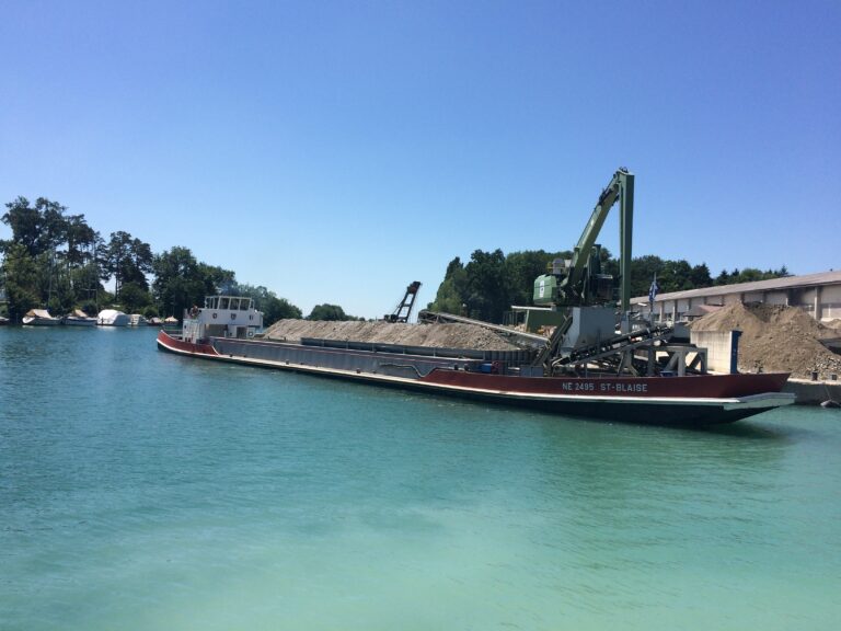 Ship carrying gravel floating along a wharf on a lake